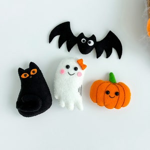 May include: A set of four felt Halloween decorations: a black cat, a white ghost, an orange pumpkin, and a black bat.