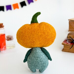 May include: A felt pumpkin character with a green stem and a teal body. The pumpkin is orange and has a fuzzy texture.