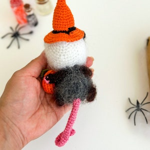 May include: A crocheted Halloween rat wearing a witch's hat and holding a pumpkin. The rat has a pink tail and is holding a small orange pumpkin.