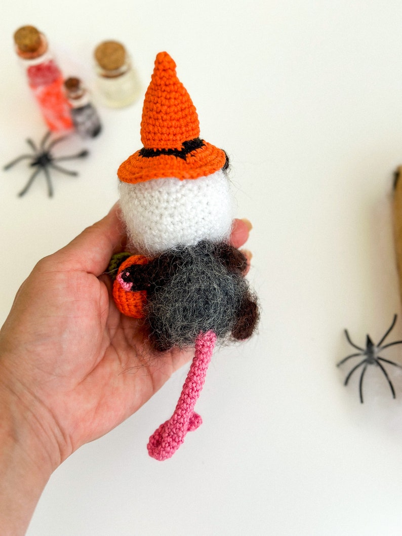 May include: A crocheted Halloween rat wearing a witch's hat and holding a pumpkin. The rat has a pink tail and is holding a small orange pumpkin.