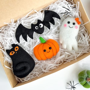 May include: A set of five felt Halloween decorations in a brown box with white shredded paper. The decorations include a black bat, a white ghost, a black cat, an orange pumpkin, and a green pumpkin.