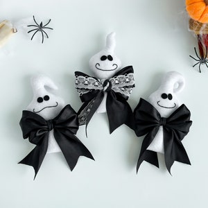 May include: Three white ghost ornaments with black bows. One ghost has a black and white lace bow. The ghosts are on a white background.