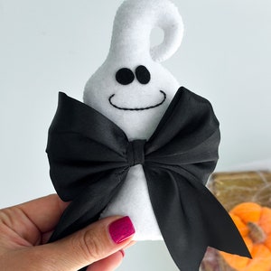 May include: White felt ghost with a black satin bow. The ghost has a smiling face with two black eyes.