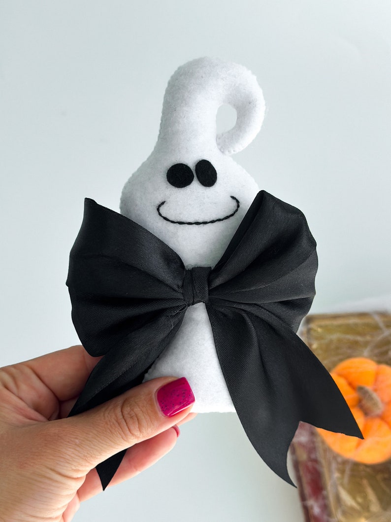 May include: White felt ghost with a black satin bow. The ghost has a smiling face with two black eyes.