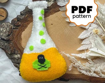 May include: A felt craft pattern for a potion bottle with a skull and crossbones design. The bottle is yellow with white and green accents. The pattern is available as a PDF download.