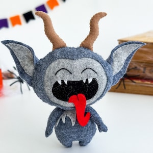 May include: A gray felt monster with horns, a wide open mouth, and a red tongue sticking out. The monster has a happy expression on its face.