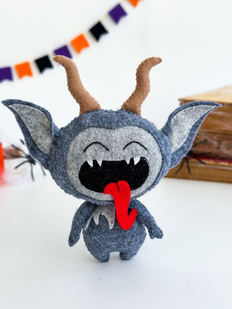 May include: A gray felt monster with horns, a wide open mouth, and a red tongue sticking out. The monster has a happy expression on its face.