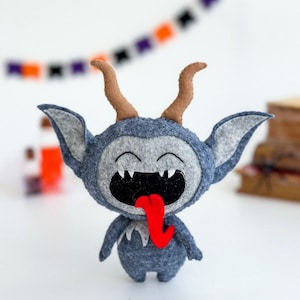 May include: A gray felt monster with horns and a big red tongue sticking out. The monster has a wide smile with white teeth.