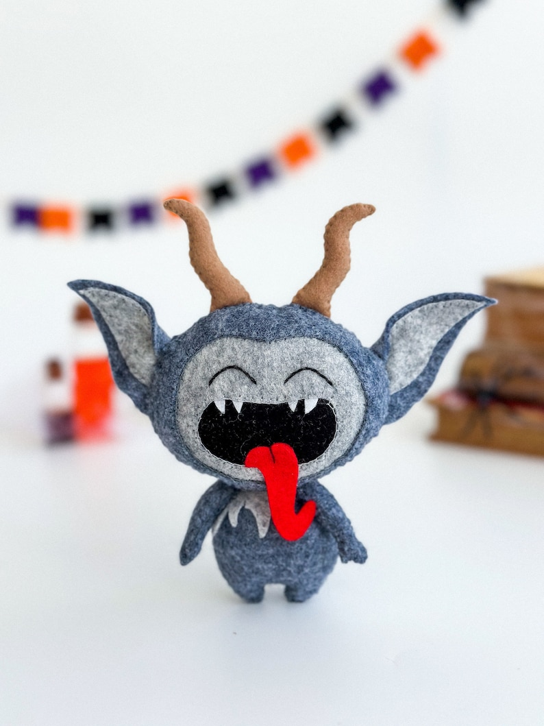 May include: A gray felt monster with horns and a big red tongue sticking out. The monster has a wide smile with white teeth.