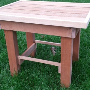 May include: A wooden table with a light brown top and a white border. The table has four legs and a shelf underneath. The table is sitting on a green grassy surface.