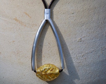 Puede incluir: Un collar de plata con un colgante de hoja de oro. El collar está hecho de dos hebras de plata que están conectadas en la parte superior e inferior. El colgante es una hoja de oro con una superficie texturizada.