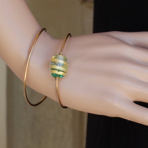 May include: A gold bangle bracelet with a green and yellow striped glass bead.
