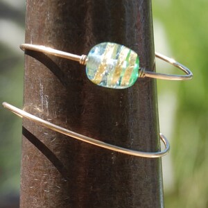 May include: A gold wire bracelet with a single green and gold glass bead.