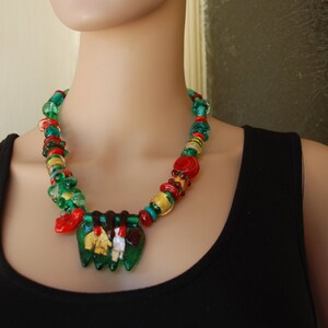 May include: A multi-colored glass bead necklace with green, red, and gold beads. The necklace has a pendant with a green, gold, and red design.