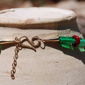 May include: A close-up of a green and red glass bead necklace with a gold clasp. The necklace is lying on a white ceramic surface.