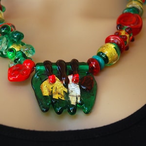 May include: A green, red, and gold glass necklace with a large green pendant featuring gold leaf accents.