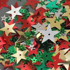 May include: A pile of shiny star-shaped sequins in red, gold, green, and silver.