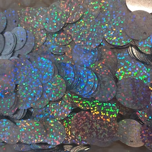 Könnte beinhalten: Nahaufnahme eines Stapels irisierender silberner Pailletten. Die Pailletten sind rund und haben eine holografische Oberfläche.