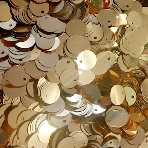 Könnte beinhalten: Ein großer Haufen goldfarbener runder Pailletten aus Metall mit einem kleinen Loch in der Mitte jeder Paillette.