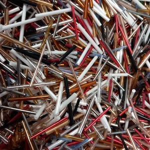 以下が含まれることがあります： 様々な形と大きさのカラフルなガラスビーズの山。ビーズはほとんどが細長く、丸いビーズが混ざっています。色は赤、オレンジ、黄色、緑、青、紫、白などです。