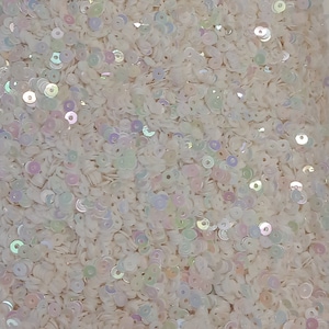 Peut inclure: Gros plan sur une pile de paillettes blanches et irisées. Les paillettes sont petites, rondes et ont un léger scintillement, reflétant une gamme de couleurs pastel. Les paillettes sont éparpillées, créant une surface texturée.