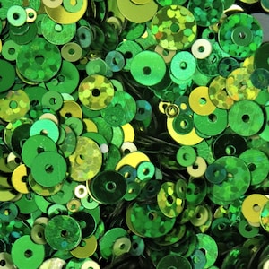 May include: A large assortment of green and yellow iridescent sequins. The sequins are various sizes and shapes, with some being round, others being oval, and some being more irregular.