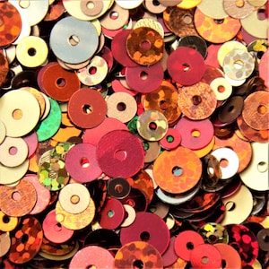 May include: Assortment of colourful round sequins in various sizes and shades of red, orange, brown, gold, and green.