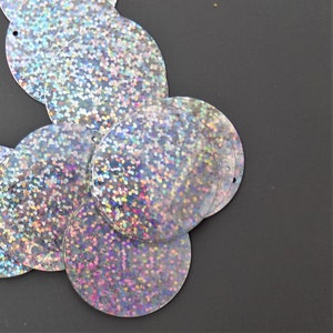 May include: A group of iridescent silver sequins with a holographic finish. The sequins are round and have a hole in the centre.