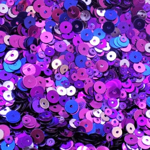 Könnte beinhalten: Eine große Auswahl an lila, rosa und blauen Pailletten. Die Pailletten sind alle in verschiedenen Größen und Formen und in einem zufälligen Muster angeordnet.