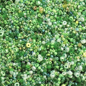 May include: A close-up image of a variety of green glass beads. The beads are of different sizes and shapes, and some have an iridescent finish.