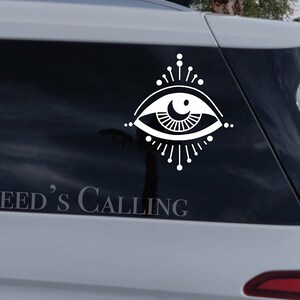 May include: White vinyl sticker of an eye with a crescent moon inside, surrounded by rays of light. The text "CREED'S CALLING" is below the eye.
