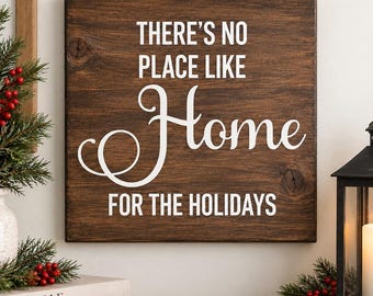 May include: A square dark brown wooden sign featuring the white text THERE'S NO PLACE LIKE Home FOR THE HOLIDAYS. The sign has a visible wood grain texture and is displayed alongside holiday decor including pine branches and a black lantern.