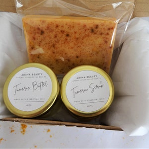 May include: A gift box filled with turmeric beauty products. The box contains a bar of turmeric soap, a jar of turmeric butter, and a jar of turmeric scrub. All products are labelled with the brand name "Ahima Beauty".