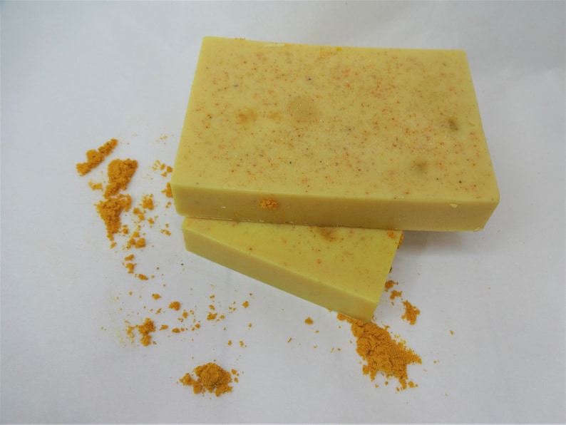 Puede incluir: Dos barras de jab&oacute;n amarillo con textura granulada, sobre una superficie blanca con polvo amarillo esparcido a su alrededor.