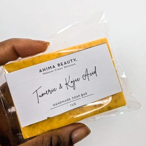 May include: A yellow bar of handmade soap with a white label that reads "AHIMA BEAUTY. Natural Clean Skincare Tumeric & Kojic Acid HANDMADE SOAP. BAR 75G"