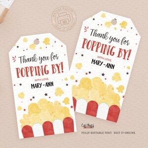 May include: Two popcorn-themed gift tags with the text "Thank you for POPPING BY!" in red and black. The tags feature a popcorn graphic and are decorated with stars. A gift box and decorative gold branch are in the background.