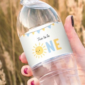 Puede incluir: Etiqueta de botella de agua con un dise&ntilde;o de sol azul y amarillo y el texto "Fun to be ONE".