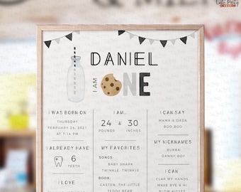 Op de afbeelding: Een afdrukbaar bord voor de eerste verjaardag van een jongen genaamd Daniel. Het bord heeft een melkfles met een koekje, een zwart-wit kleurenschema en een banner met vlaggen. Het bord bevat details over Daniels geboorte, gewicht, lengte, favoriete dingen en wat hij kan doen.