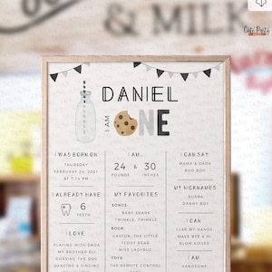 May include: A printable first birthday sign for a boy named Daniel. The sign features a milk bottle with a cookie, a black and white color scheme, and a banner with flags. The sign includes details about Daniel's birth, weight, height, favorite things, and what he can do.