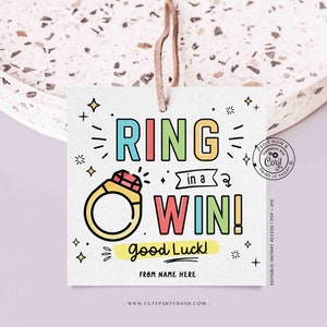 May include: A colorful printable tag with the text "RING in a WIN! Good Luck!" and a cartoon ring with a red gem. The tag is decorated with stars and plus signs.