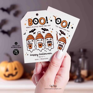 以下が含まれることがあります： オレンジ色の「BOO！」の文字が入った、白いハロウィーンのギフトタグ2枚。オレンジ色の帽子をかぶり、コーヒーカップを持ったお化けのイラストが描かれています。タグには「Here's a little treat for you!」と「Happy Halloween」と書かれています。