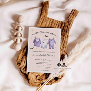 Pu&ograve; includere: Un invito per un baby shower con il testo "a little boo is almost due!" presenta illustrazioni di vestiti per bambini e un fantasma. L'invito &egrave; su sfondo rosa, con una tutina marrone e un sonaglio di legno.