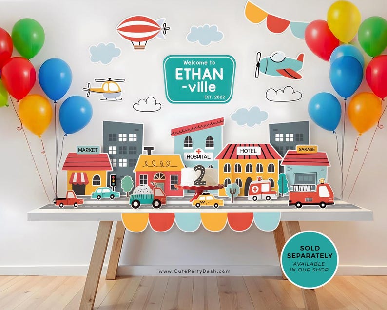 May include: A birthday party decoration set with a city theme. The set includes a banner that says "Welcome to Ethan-ville Est. 2022", a cake topper with the number 2, and various buildings, vehicles, and balloons. The colors are bright and cheerful, with red, blue, yellow, and green being prominent.