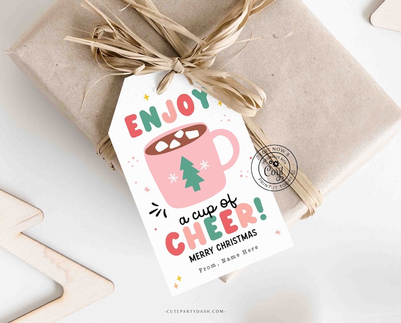 May include: A white gift tag with a pink and green illustration of a mug of hot chocolate with marshmallows. The text on the tag reads "Enjoy a cup of Cheer! Merry Christmas. From, Name Here."