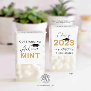 May include: Two small white boxes of mints with graduation themed labels. The left box has a black graduation cap and gold text that says "Outstanding Achieve Mint". The right box has a gold graduation cap and gold text that says "Class of 2023 congratulating Nicole Garder".