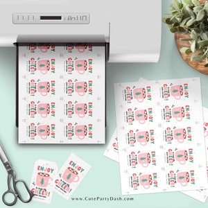 May include: Printable gift tags featuring a pink mug with marshmallows and a green Christmas tree. The text on the tags reads "Enjoy a cup of cheer! Merry Christmas".
