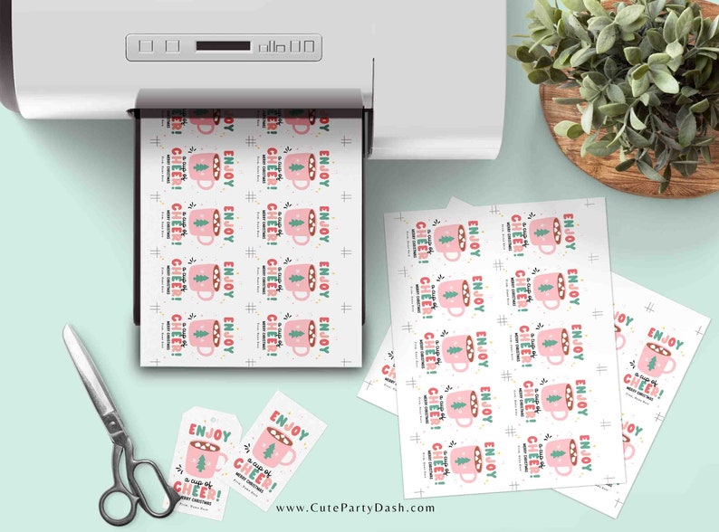 May include: Printable gift tags featuring a pink mug with marshmallows and a green Christmas tree. The text on the tags reads "Enjoy a cup of cheer! Merry Christmas".