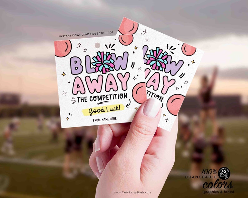 May include: Two square gift tags with the text "BLOW AWAY THE COMPETITION" in purple and pink. The tags have a pom-pom graphic and the words "Good Luck!" and "From, Name Here". The tags are held in a hand.