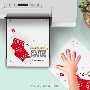 May include: A printable Christmas card with a red stocking and the text "Wishing you a season stuffed with joy!"  The card is being printed on a white printer.