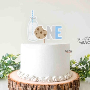 May include: Printable cake topper featuring a milk bottle with a straw, a cookie, and the word "ONE" in blue and gray letters. The topper is approximately 6 inches wide.